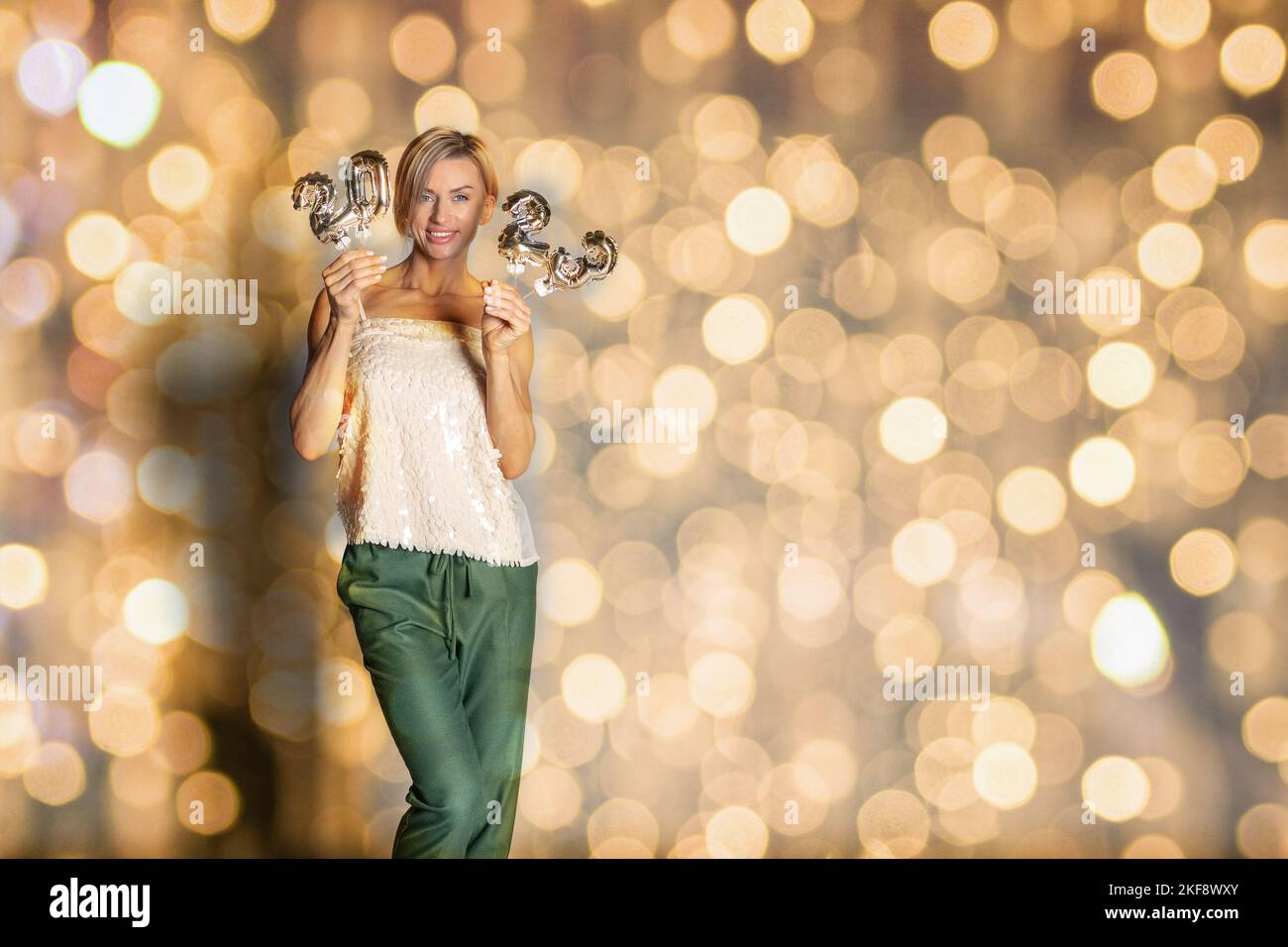 Happy New Year 2023 celebration. Female holding golden balloons in form of numbers on shiny bokeh lights on festive on yellow background. High quality photo Stock Photo