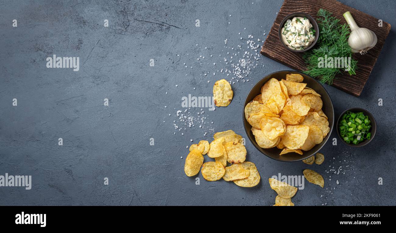Crispy potato chips with herbs, salt and sour cream on a graphite
