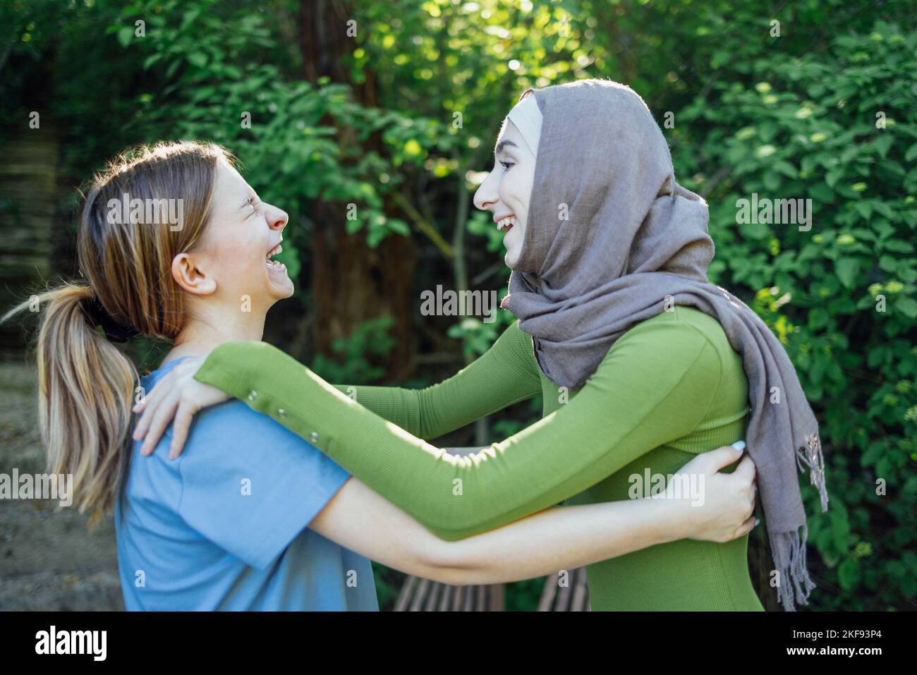 Strong female friendship. Happy two teen girls best friends holding hands and hugging while standing in front of park. Multiethnical friends Stock Photo