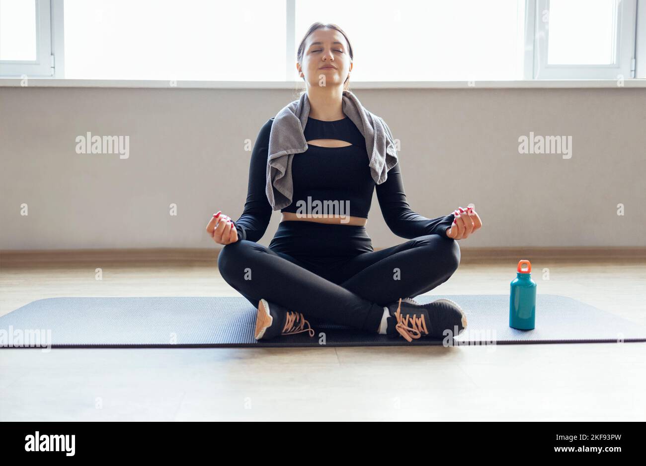 Young attractive happy woman practicing yoga, doing Padmasana exercise, Lotus pose with mudra, working out, wearing sportswear, white tank top, indoor Stock Photo