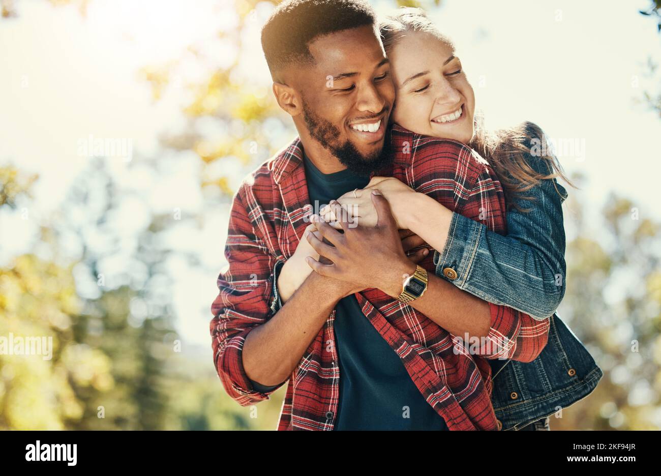 Love, nature and diversity couple hug on outdoor journey together, romantic park date and quality time fun. Sunshine flare, leaf and summer freedom Stock Photo