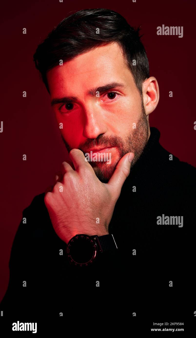 Model, face and portrait of man for beauty, skincare and fashion on a red studio background. Trendy, edgy and stylish guy front for cool facial health Stock Photo