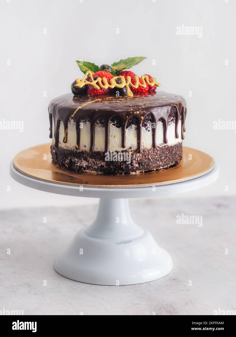 dark chocolate drips birthday sweet cake, fresh fruits Raspberry strawberry blueberry cranberry on top, decorated with golden edible paint Stock Photo