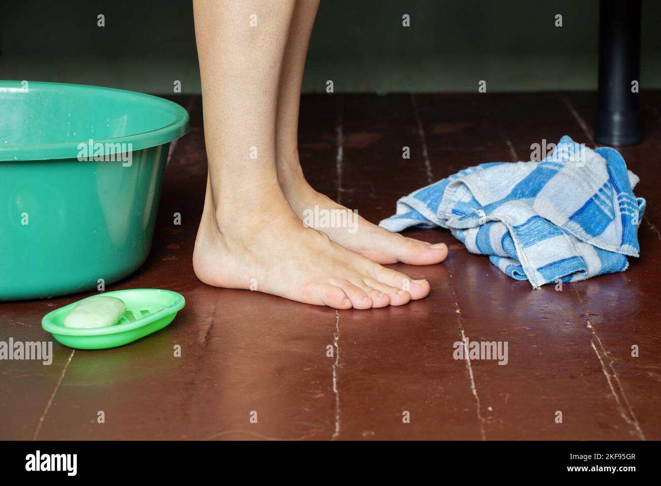 girl washes her feet in a bowl of water on the wooden floor at home, foot care, wash feet at