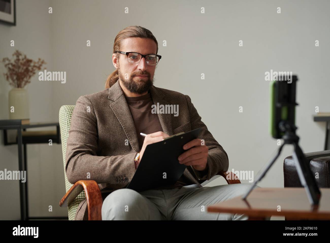 Serious psychologist sitting on armchair in front of mobile phone in