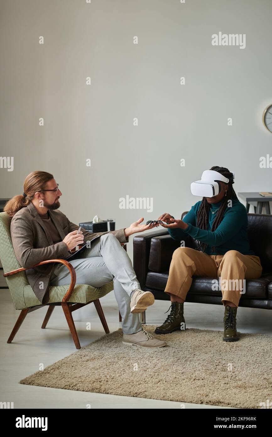 African American patient in virtual reality glasses trying to overcome her fear with virtual teleportation Stock Photo