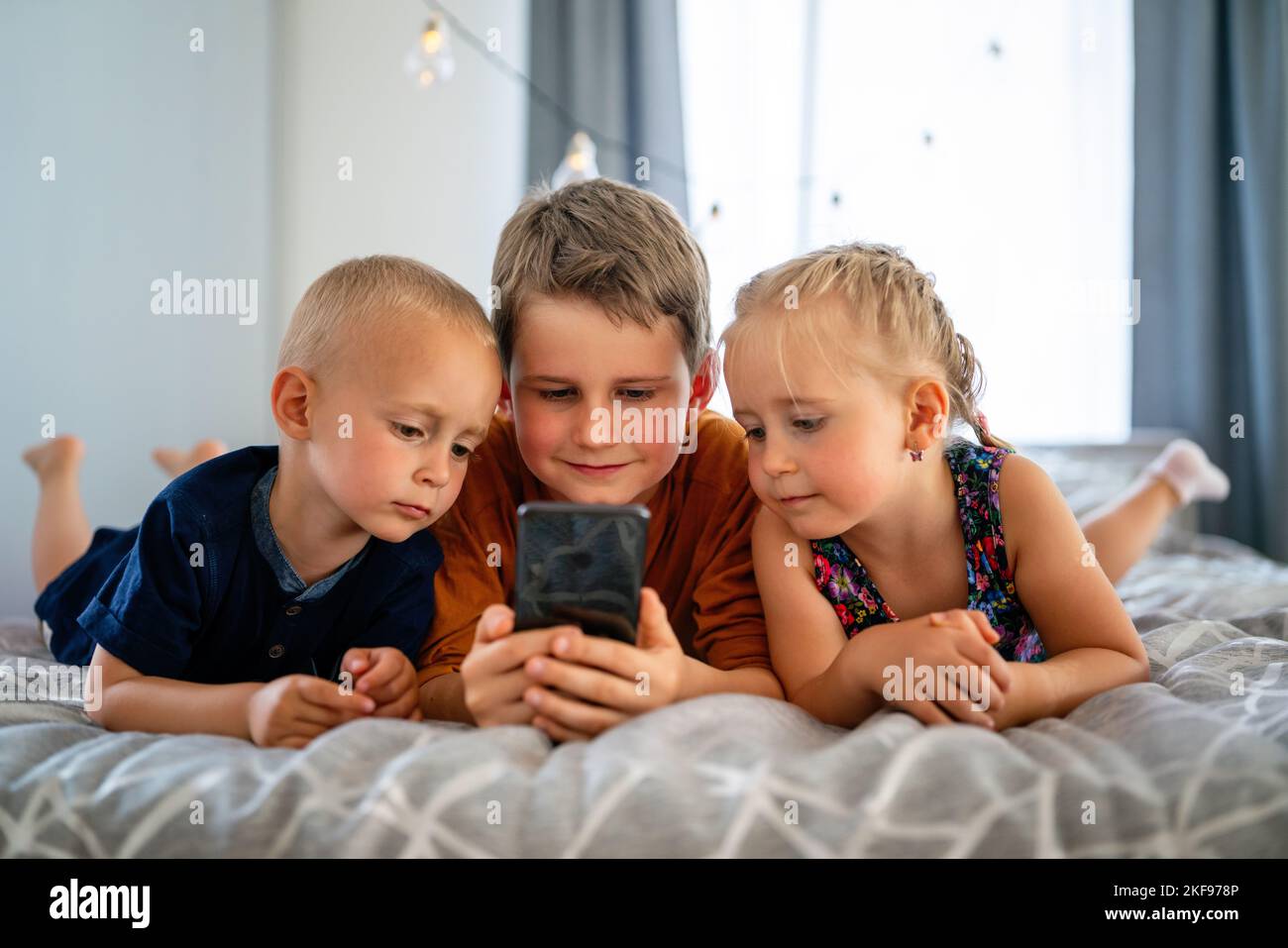 Portrait of children playing on mobile phone together at home. Internet and network addiction. Stock Photo