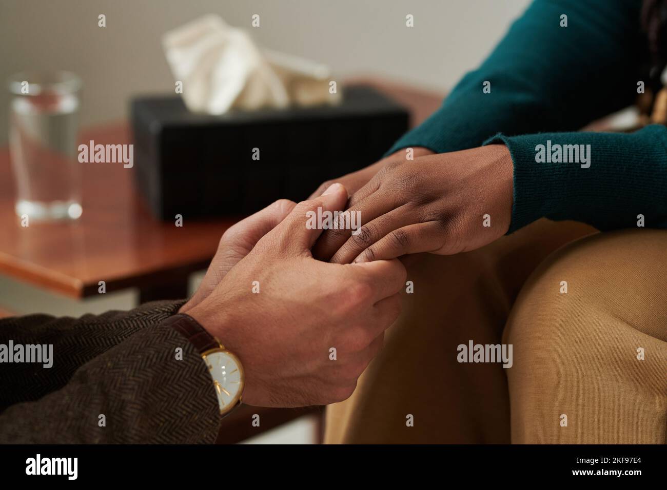 Close-up of psychologist holding hands with patient and supporting her during psychotherapy at office Stock Photo