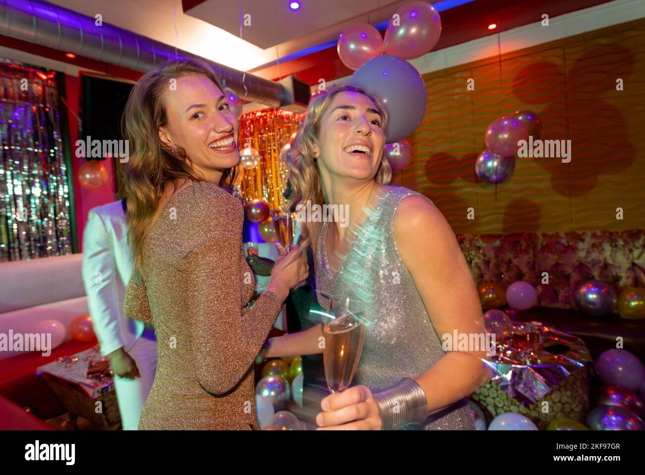 Two happy caucasian female friends laughing and drinking glasses of champagne at a nightclub. Fun, drinking, going out, friendship and party concept. Stock Photo