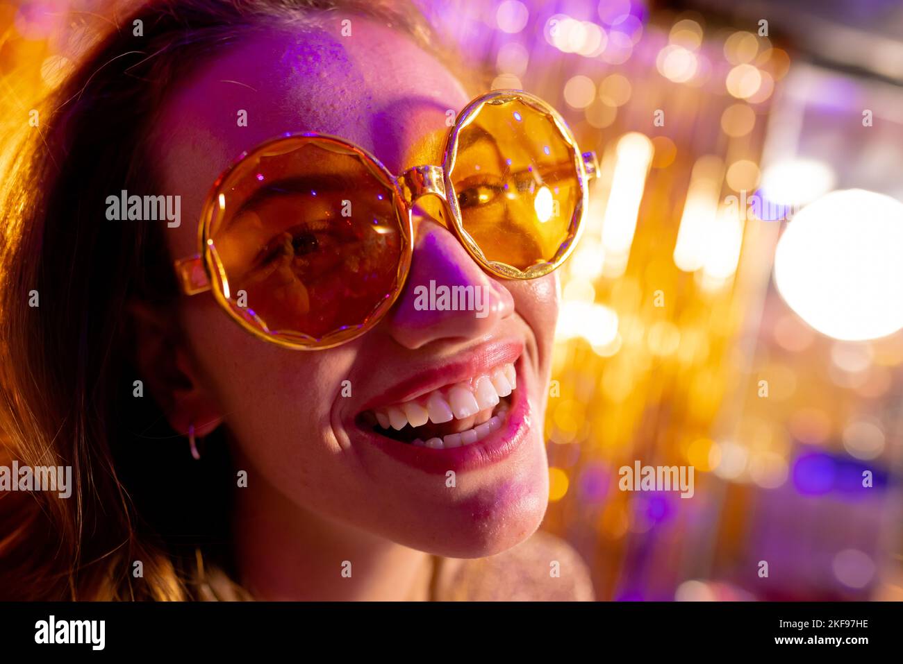 Close up portrait of happy caucasian woman wearing sunglasses smiling to camera at a nightclub. Fun, going out and party concept. Stock Photo