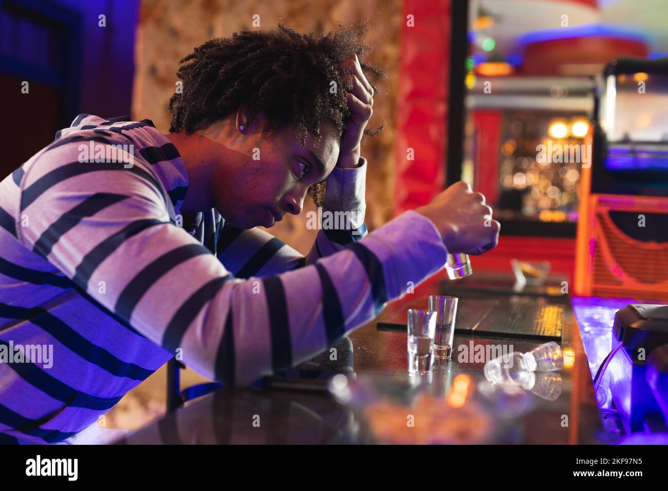 Drunk african american man holding head sitting at bar drinking shots Stock Photo