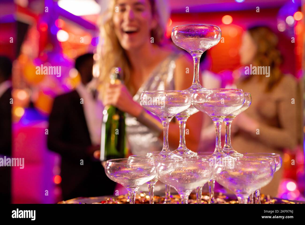 Happy caucasian woman preparing to pour champagne into pyramid of glasses at a party in a nightclub. Fun, drinking, going out and party concept, selec Stock Photo