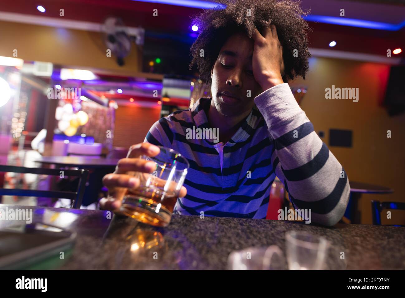 Drunk african american man sitting holding head at the bar drinking in a bar Stock Photo