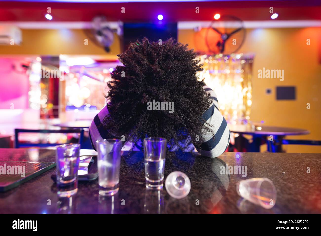 Drunk african american man sitting at the bar with head down and empty shot glasses Stock Photo