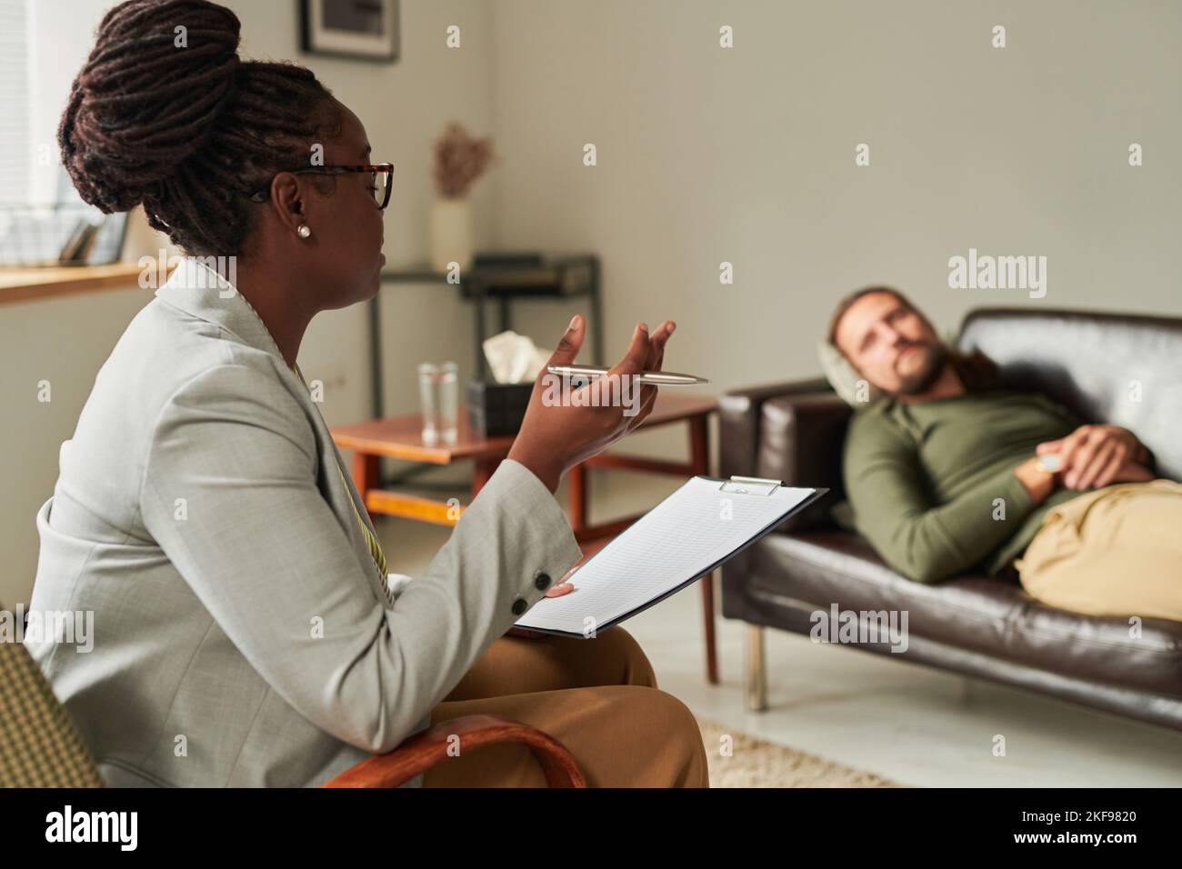 African American psychologist with document sitting on armchair and talking to patient at office Stock Photo