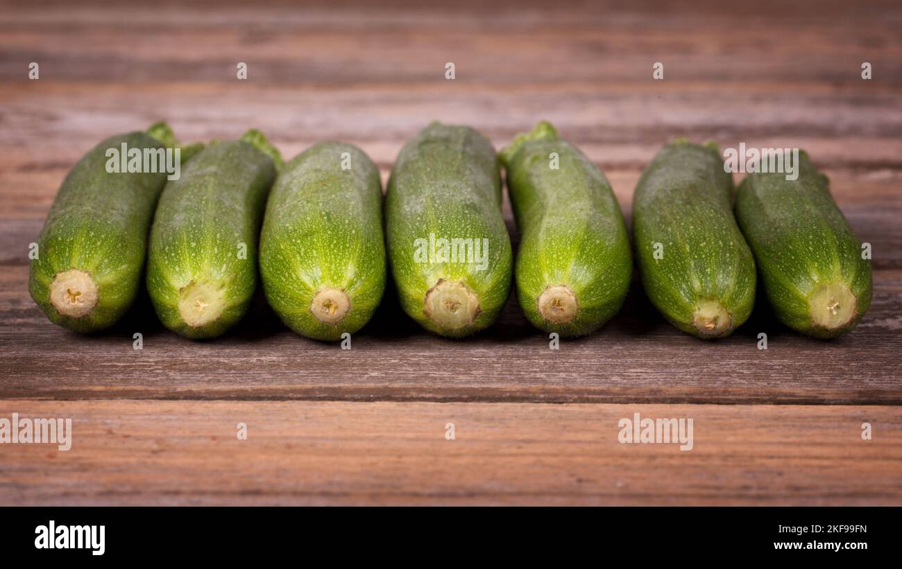 A row of frsh courgetters on an old wood table. Stock Photo