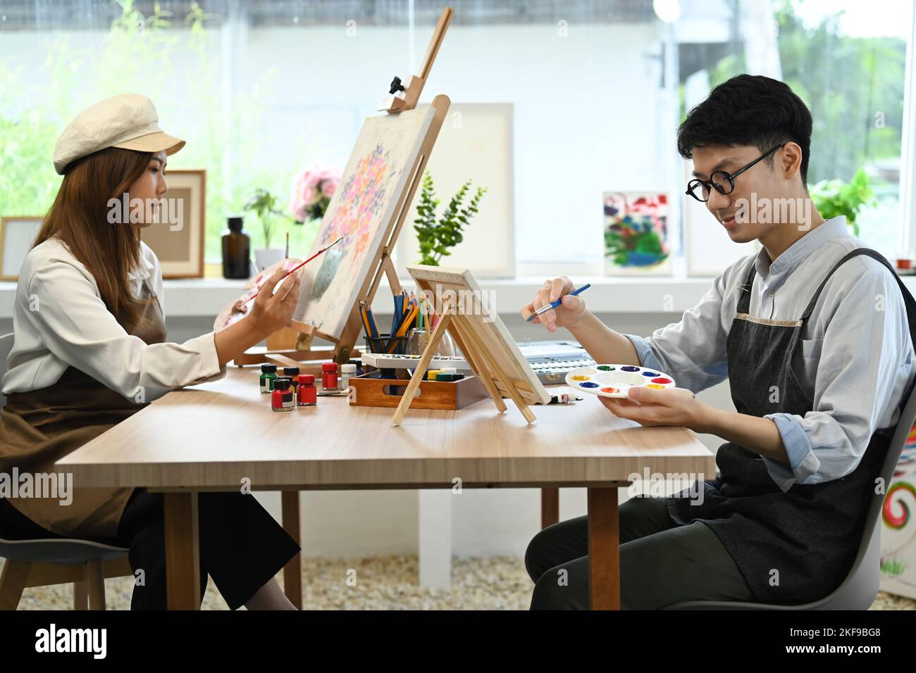 Two young art students painting with acrylic paints on canvas working together in bright studio. Artistic and education concept Stock Photo