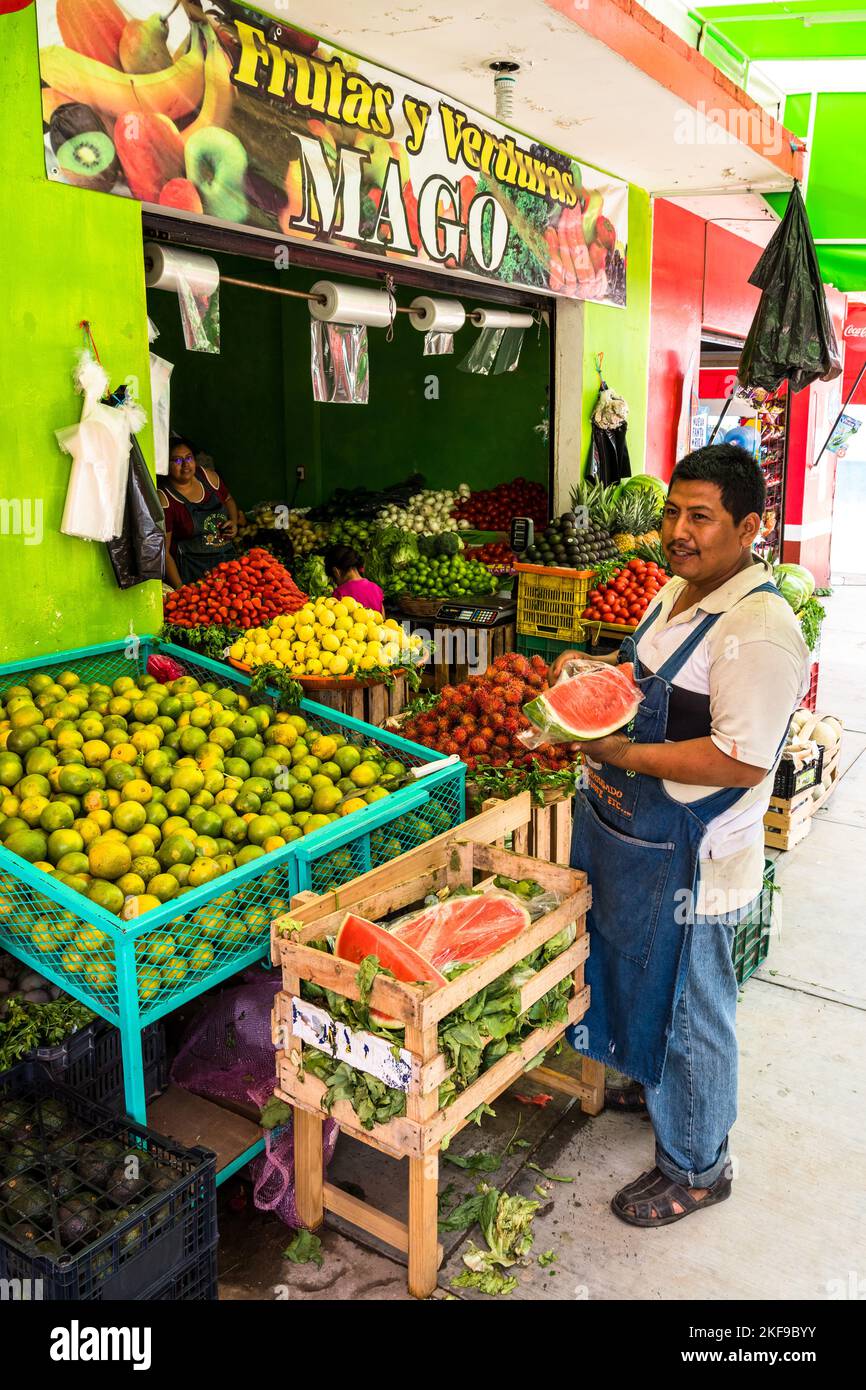 A vendor stands in front of his shop selling fruits and vegetables
