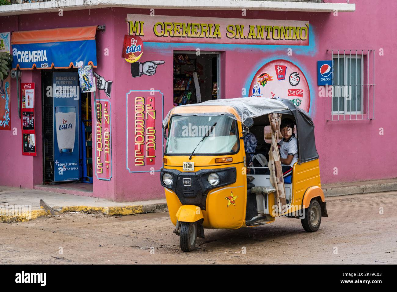 A mototaxi carries passengers in front of a neighborhood shop in San
