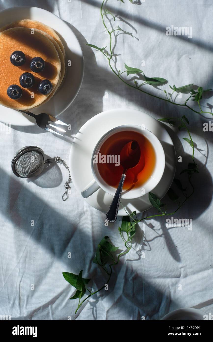 Blueberry pancakes with tea, white tablecloth, copy space, shabby chic flatlay Stock Photo