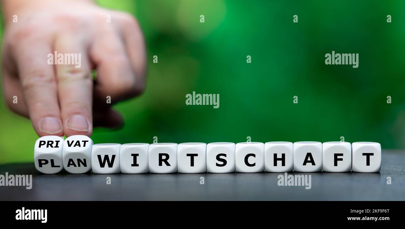 Hand turns dice and changes the German expression 'Planwirtschaft' (state-directed economy) to 'Privatwirtschaft' (private economy). Stock Photo