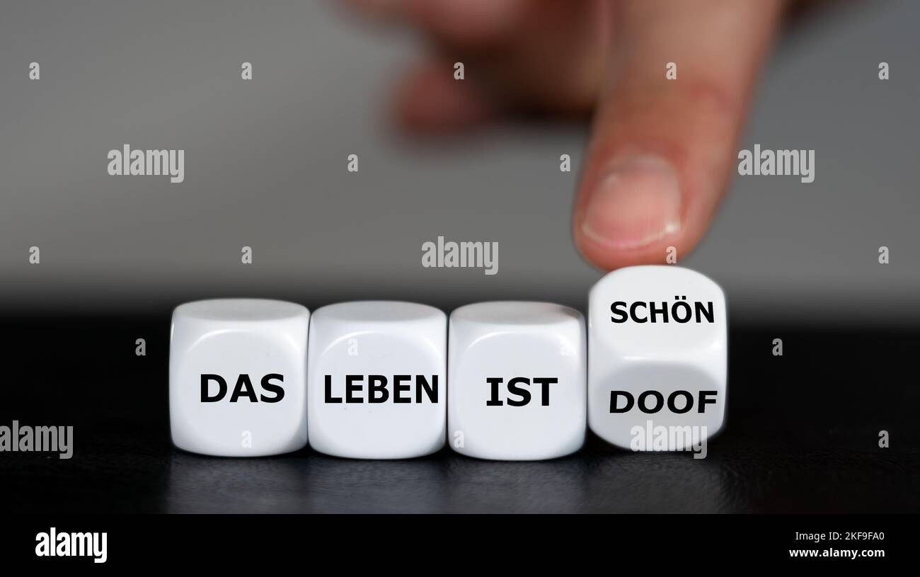 Concept to change the attitude. Hand turns dice and changes the German expression 'das Leben ist doof' (life is bad) to 'das Leben ist schön' (life is Stock Photo