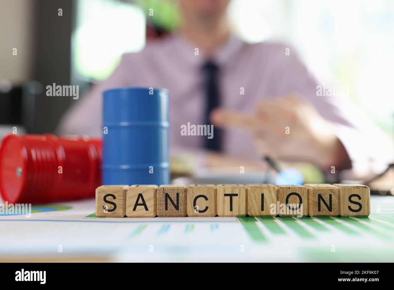 Oil drums on financial statements, word sanction and business man in background. Stock Photo