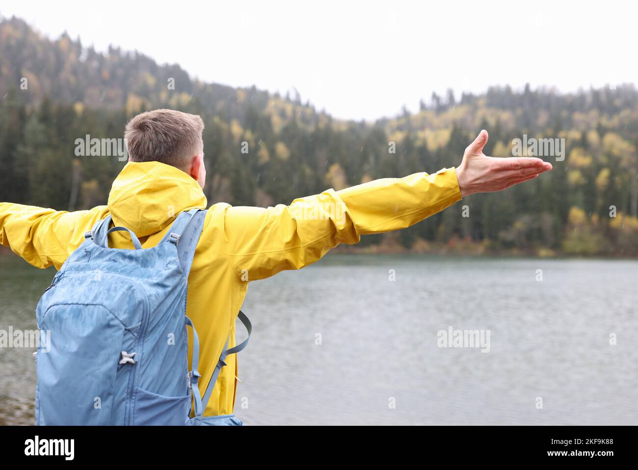 Young casual traveler with backpack looks into the distance at lake and mountains. Stock Photo