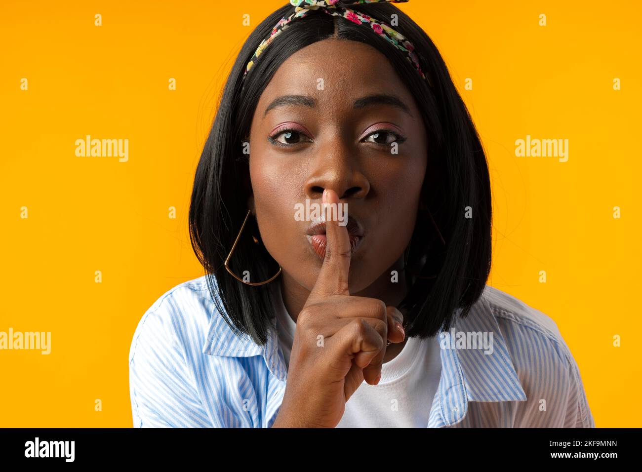 Young african woman asking to be quiet with finger on lips against yellow background Stock Photo