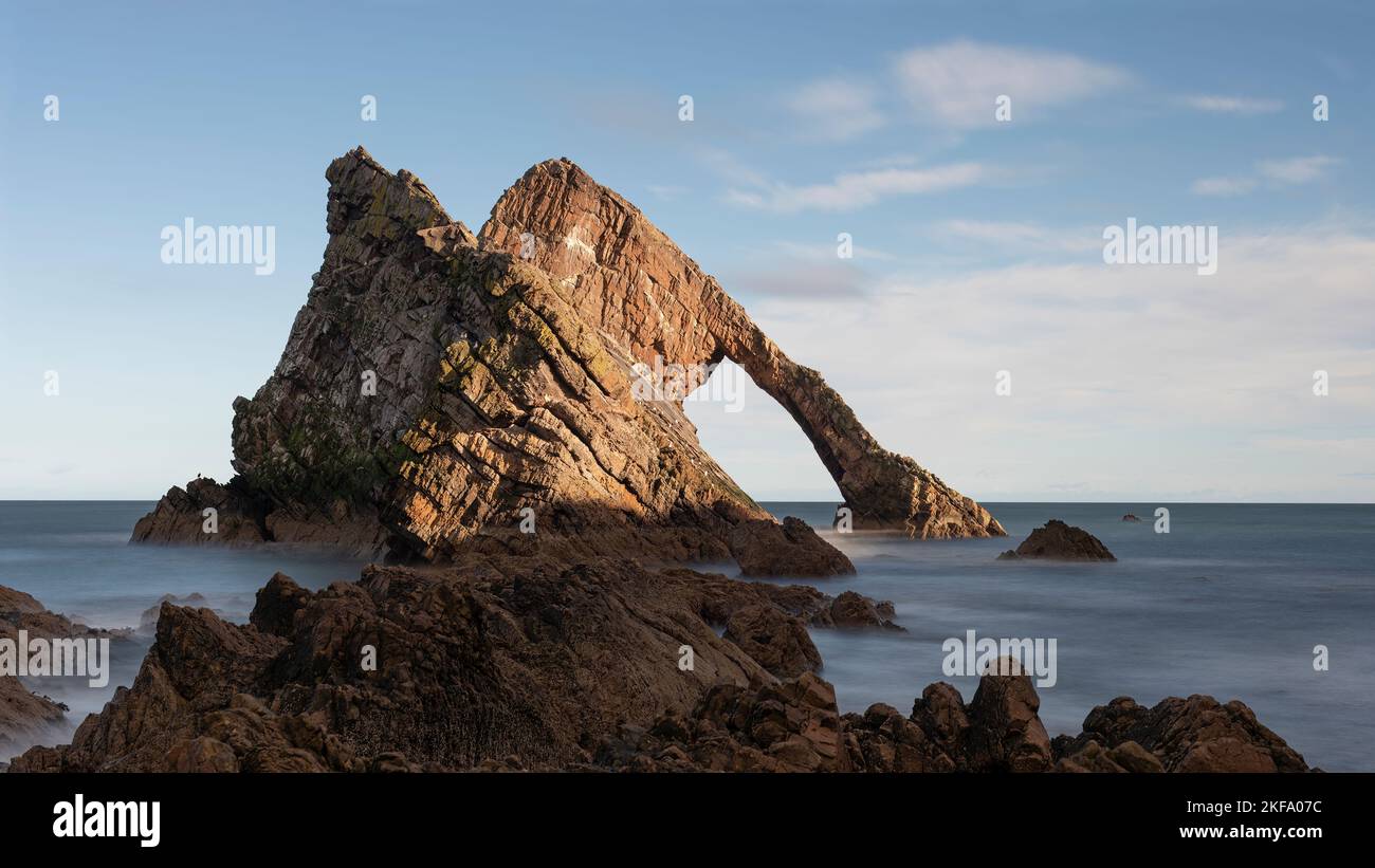 Bow Fiddle Rock in the Scottish highlands. Bow shaped carved into the rock face. Slow shutter to create smooth water rolling over the pebble beach. Be Stock Photo