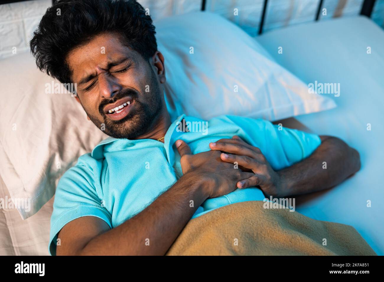 young Indian man got sudden chest pain while in deep sleep at night - concept of healthcare, illness and heart ache. Stock Photo