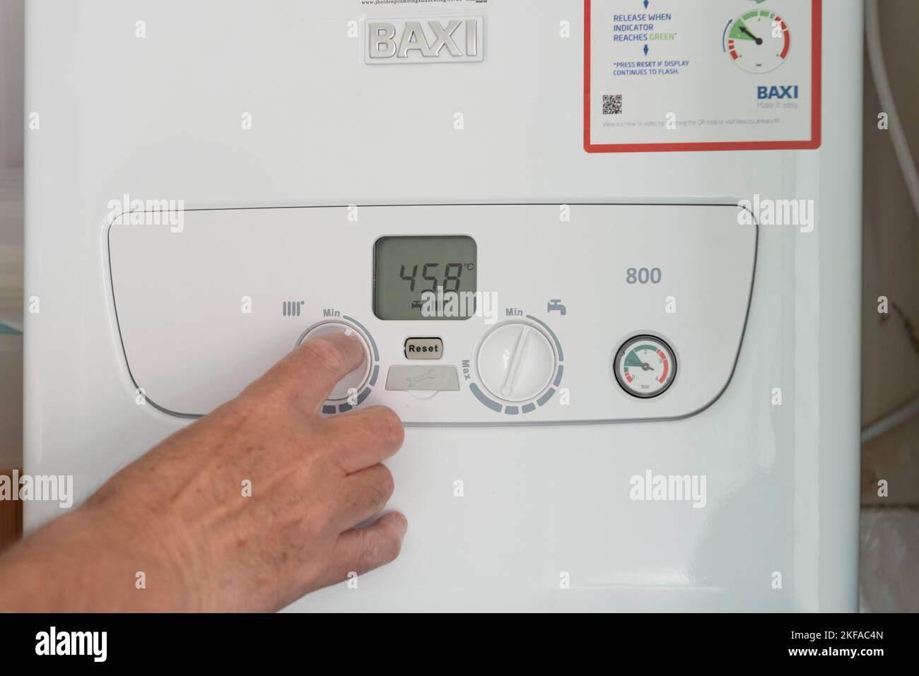 Man's hand turning down the dial on a boiler unit heating system Stock