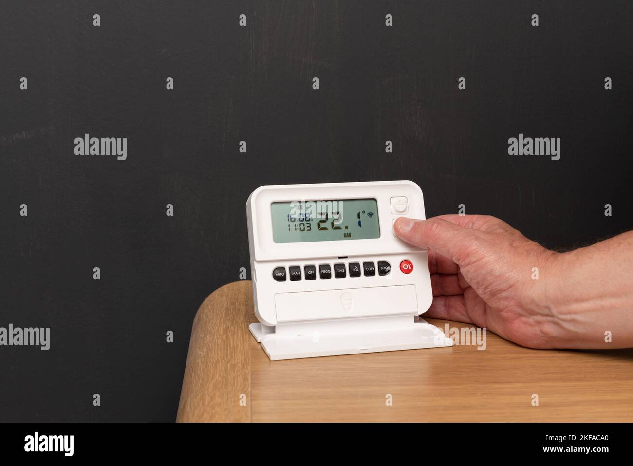 Photo of man's hand turning down the thermostat control for the boiler central heating system. Cost of living crisis in the UK Stock Photo