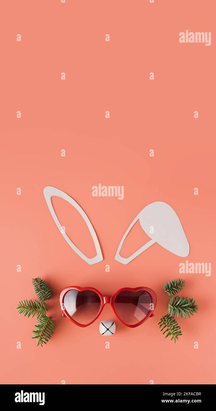 Minimalistic Christmas composition. Bunny face made from paper ears, heart shaped glasses, Christmas bell and spruce branches. Flat lay. 2023 year of Stock Photo