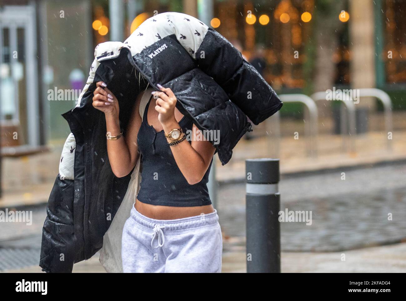 Young girl holding PLAYBOY anorak over her head in Preston, Lancashire.  UK Weather 17 Nov 2022.   Wet and Windy weather for shoppers in the city centre.  Credit; MediaWorldImages/AlamyLiveNews Stock Photo