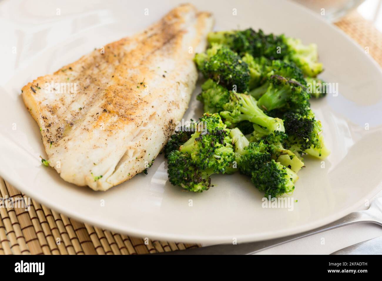 fried fillet of sea bass with garnish of broccoli on black warm stone