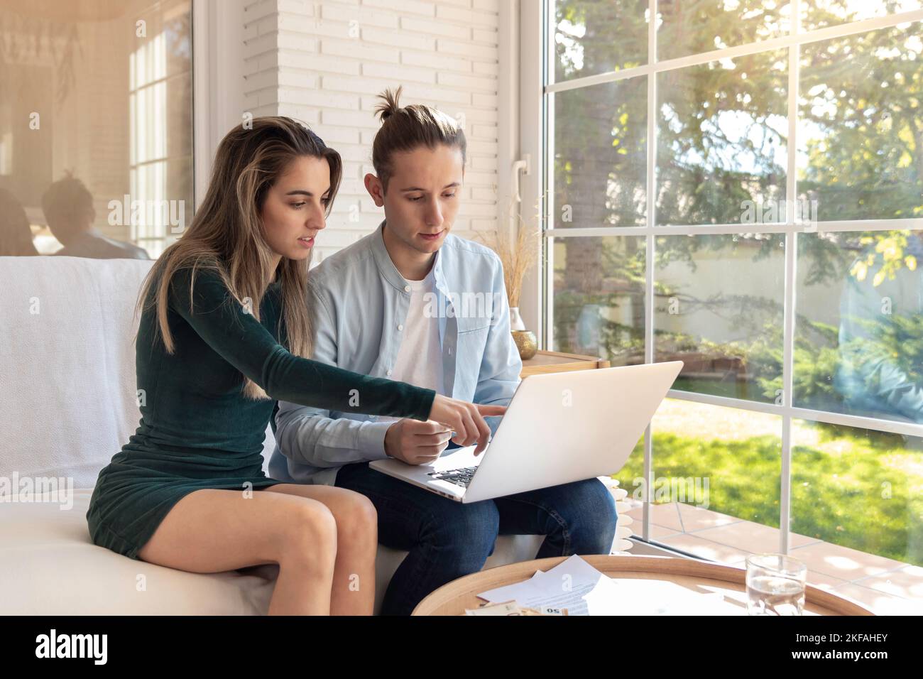 Young couple revising the financial for home budget revision concept in the laptop sitting in the sofa in the living area at home Stock Photo
