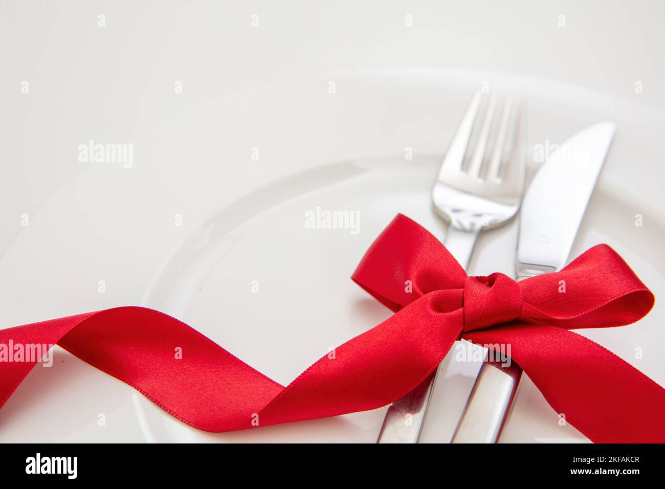 Holiday table setting close up view. Cutlery and red satin ribbon decoration on white dishes, Christmas, Valentines day celebration dinner Stock Photo