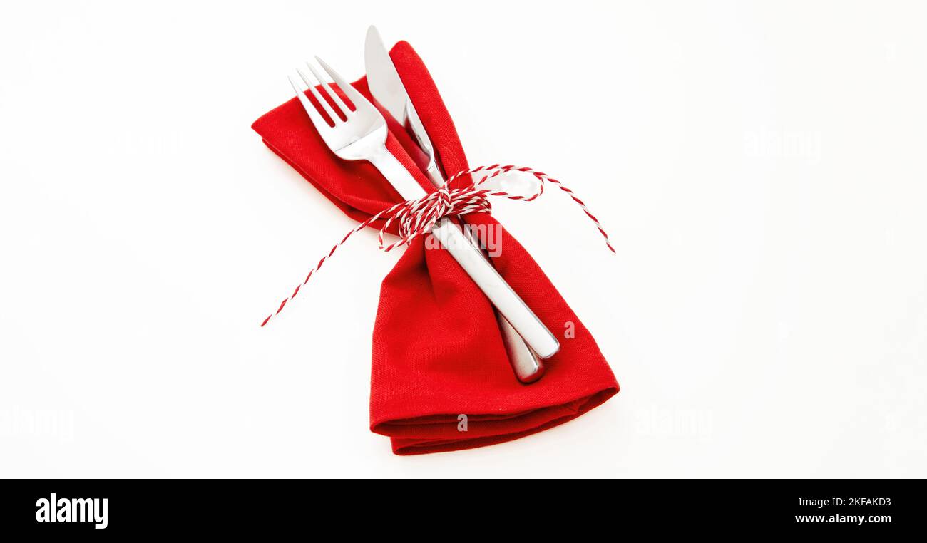 Holiday table setting, celebration dinner. Cutlery, red cloth napkin and Christmas twine string bow isolated on white, close up view. Stock Photo
