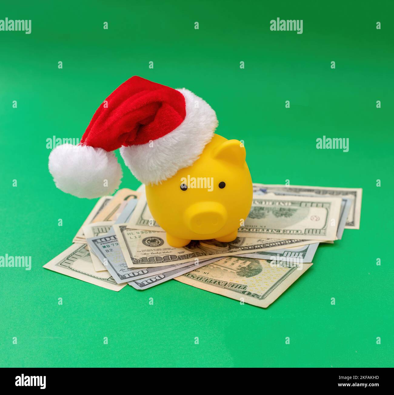 Christmas holiday bonus and expenses. Piggy bank with Santa hat on US dollars money pile, green background. Stock Photo