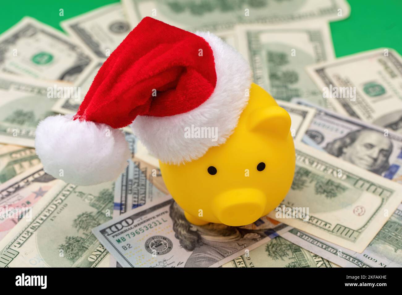 Christmas holiday bonus and expenses. Piggy bank with Santa hat on US dollars money pile background, above view. Stock Photo