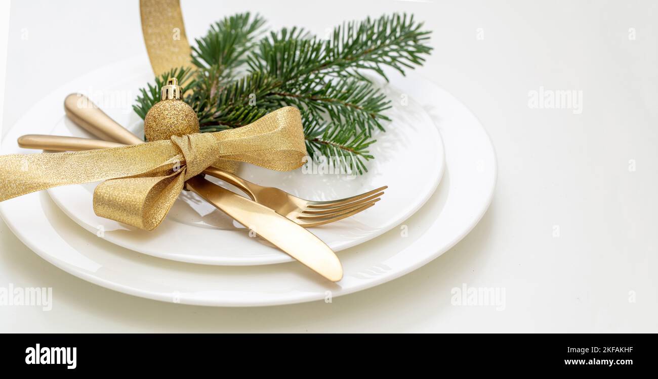 Christmas table setting close up view. Gold cutlery and fir decoration on white dishes, New Year celebration dinner Stock Photo