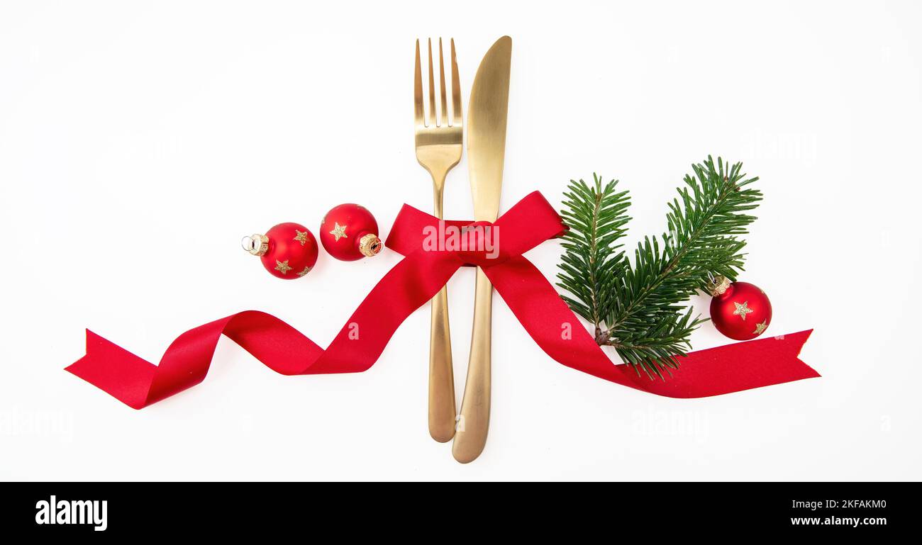 Christmas holiday celebration dinner. New Year table setting isolated on white. Golden cutlery, Xmas decoration and red ribbon top view. Stock Photo