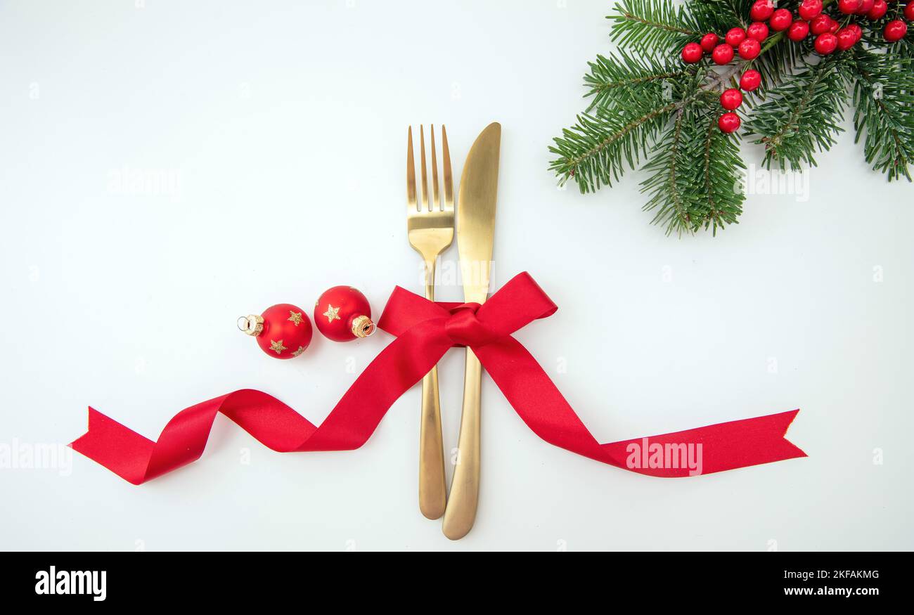 Christmas holiday celebration dinner. New Year table setting. Golden cutlery, Xmas decoration and red ribbon top view. Stock Photo