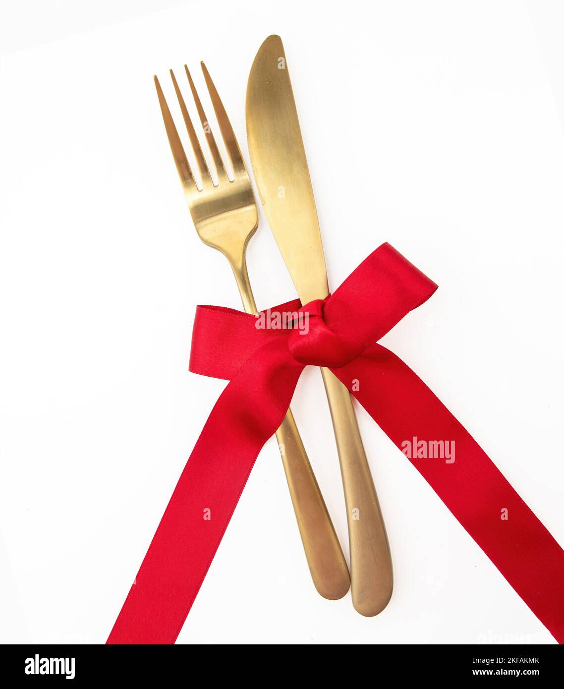 Holiday table setting top view. Golden fork and knife and red satin ribbon decoration isolated on white. Christmas, Valentines day celebration dinner Stock Photo