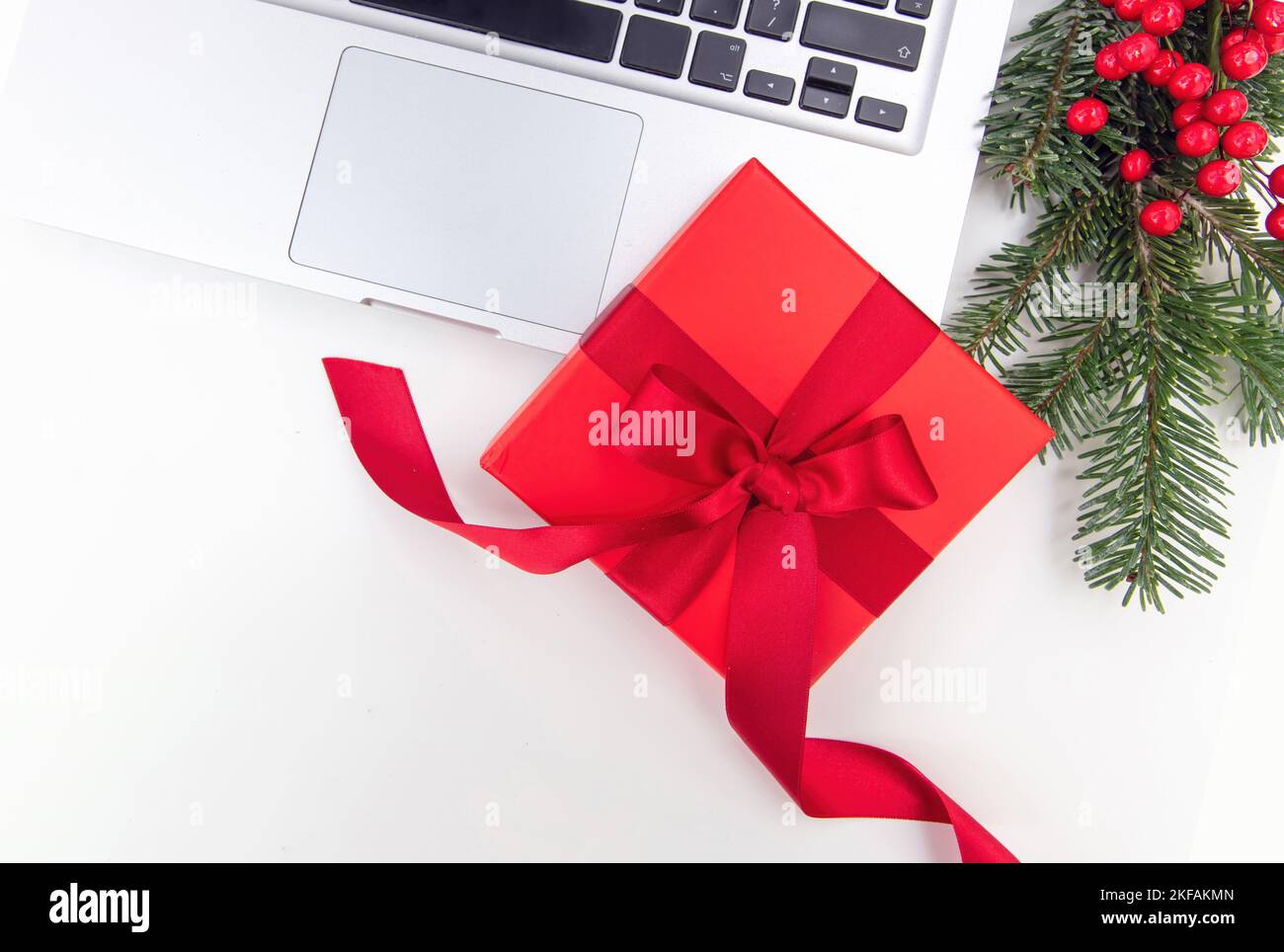 Christmas Holiday. Red gift box, computer laptop and Xmas decoration on white background, top view, copy space. Stock Photo