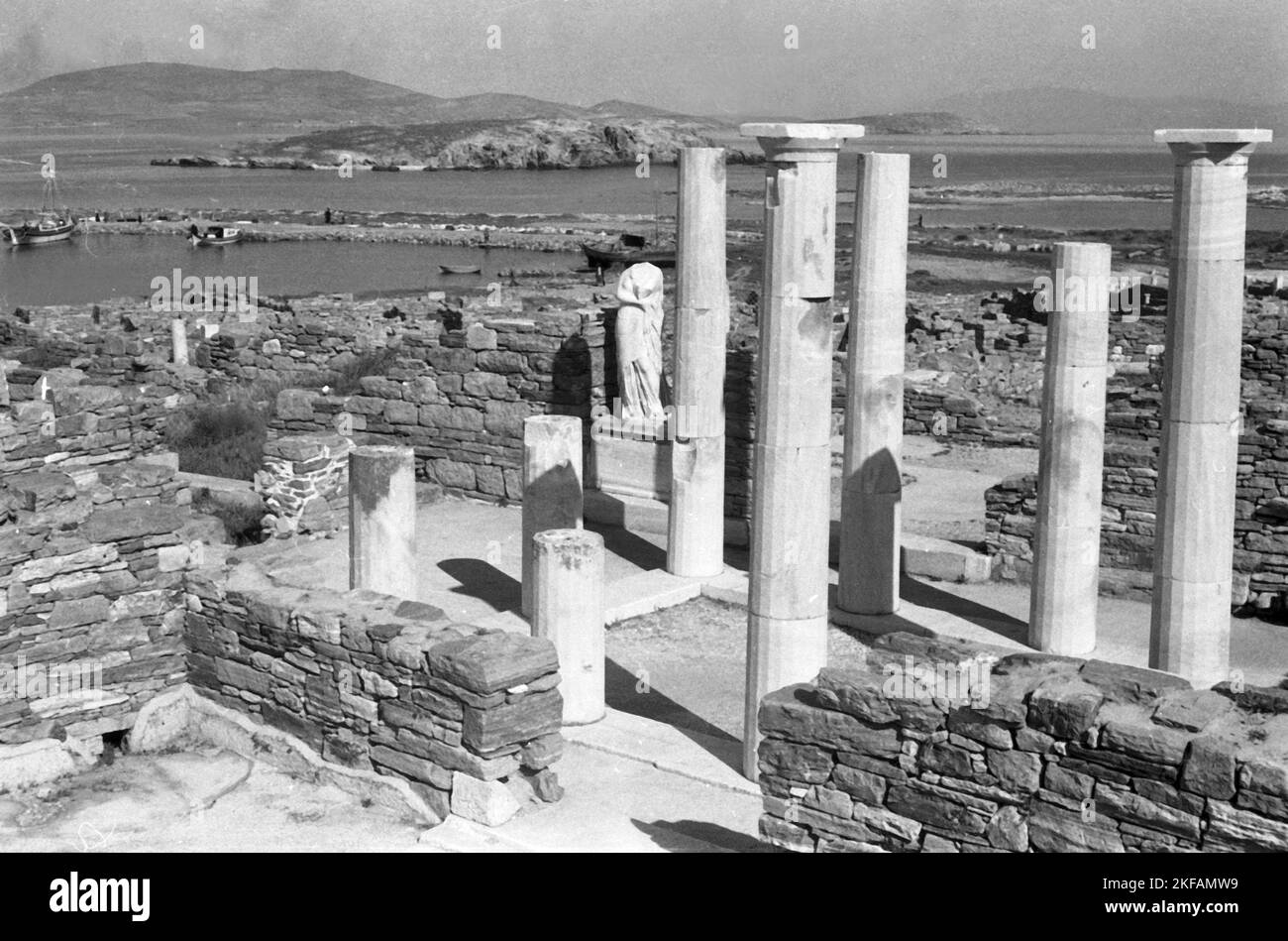Griechenland - Ein interessanter Kontrast: Blick über die Ruinen der Insel Delos, Kykladen, auf das moderne Kreuzfahrtschiff, das in der Bucht ankert, 1954. Greece - An interesting contrast: View over the ruins of Delos island, Cyclades, to the modern cruise linern anchoring in the bay, 1954. Stock Photo