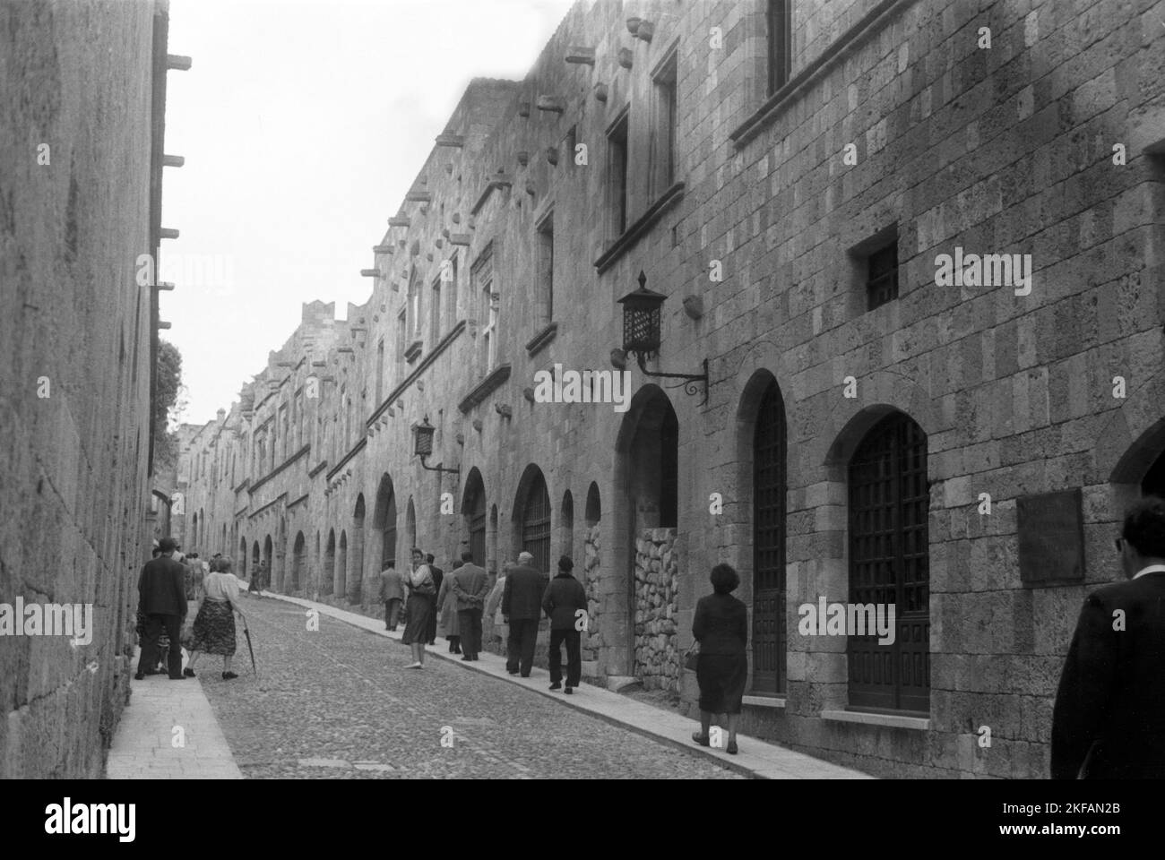 Eine Straße mit Kopfsteinpflaster führt an einem robusten Gebäudekomplex entlang, Griechenland, 1950er Jahre. A cobblestoned street near a castle like buidling in Greece, 1950s. Stock Photo