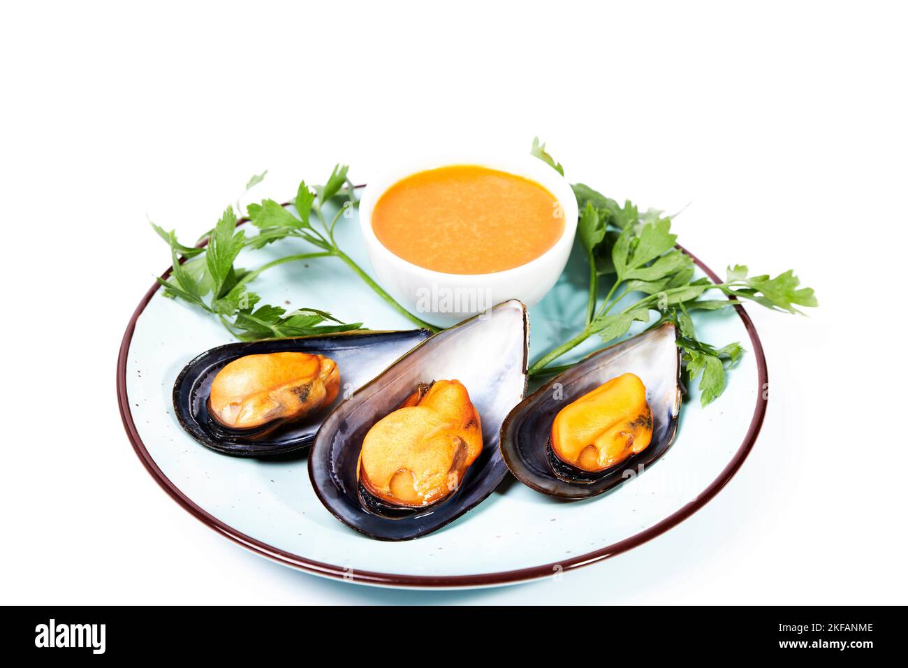 Dish with steamed mussels with parsley and a bowl of spicy sauce on a white background. Shell food. Healthy food Stock Photo