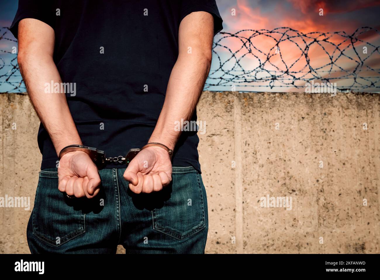 Criminal in jail. A handcuffed man stands against a barbed wire wall